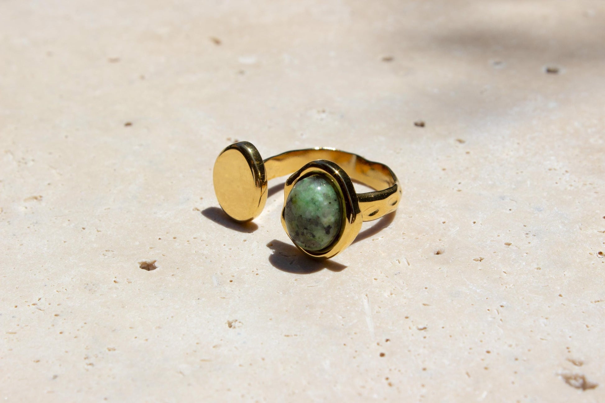 green gemstone ring on gold ring on concrete.