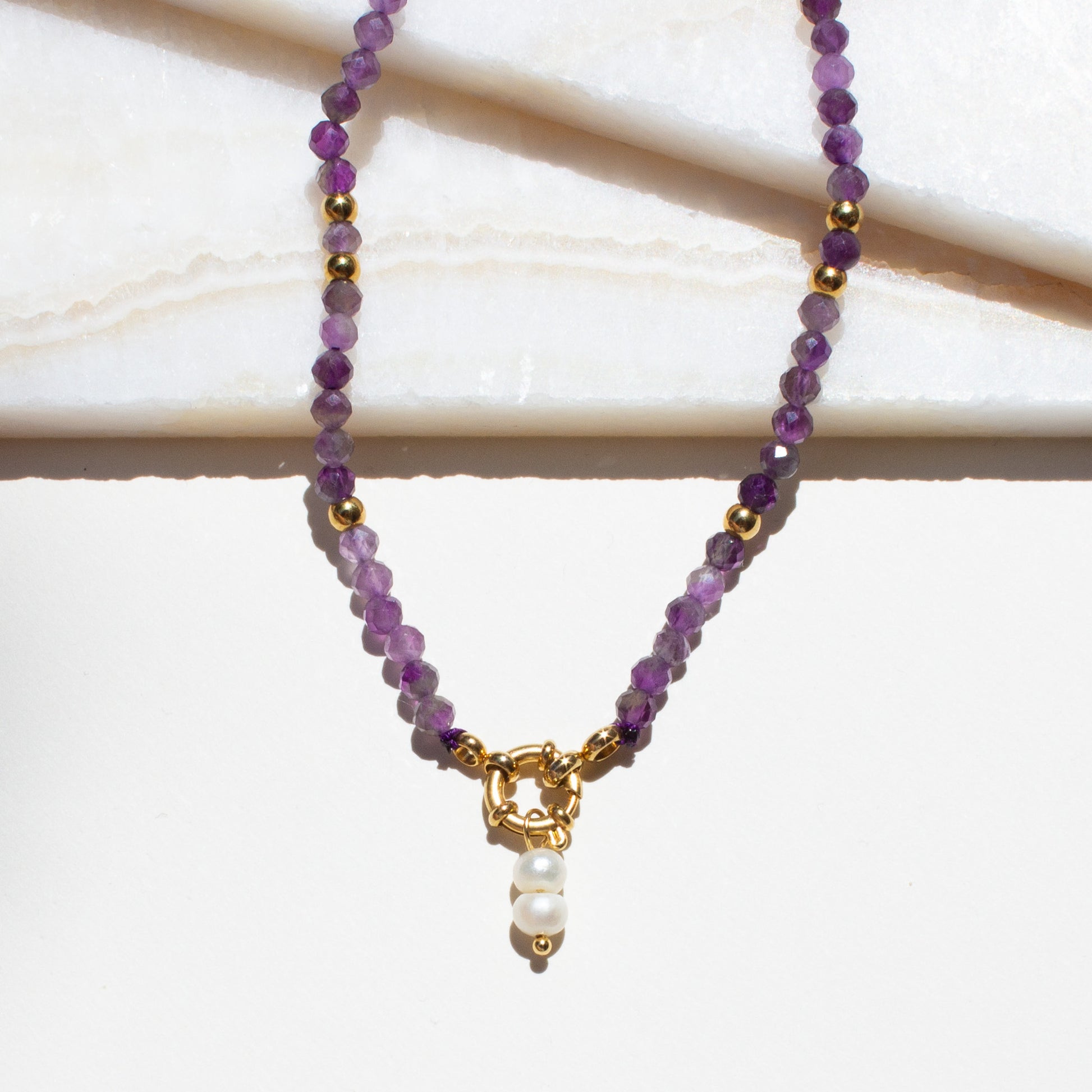 Purple amethyst beaded necklace with a gold clasp and pearl accent on a white background.