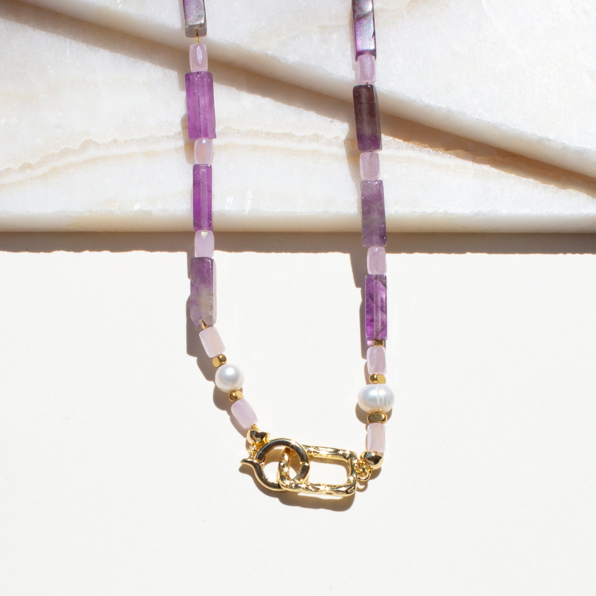 Necklace with purple and pink amethyst beads and a gold clasp on a white background.