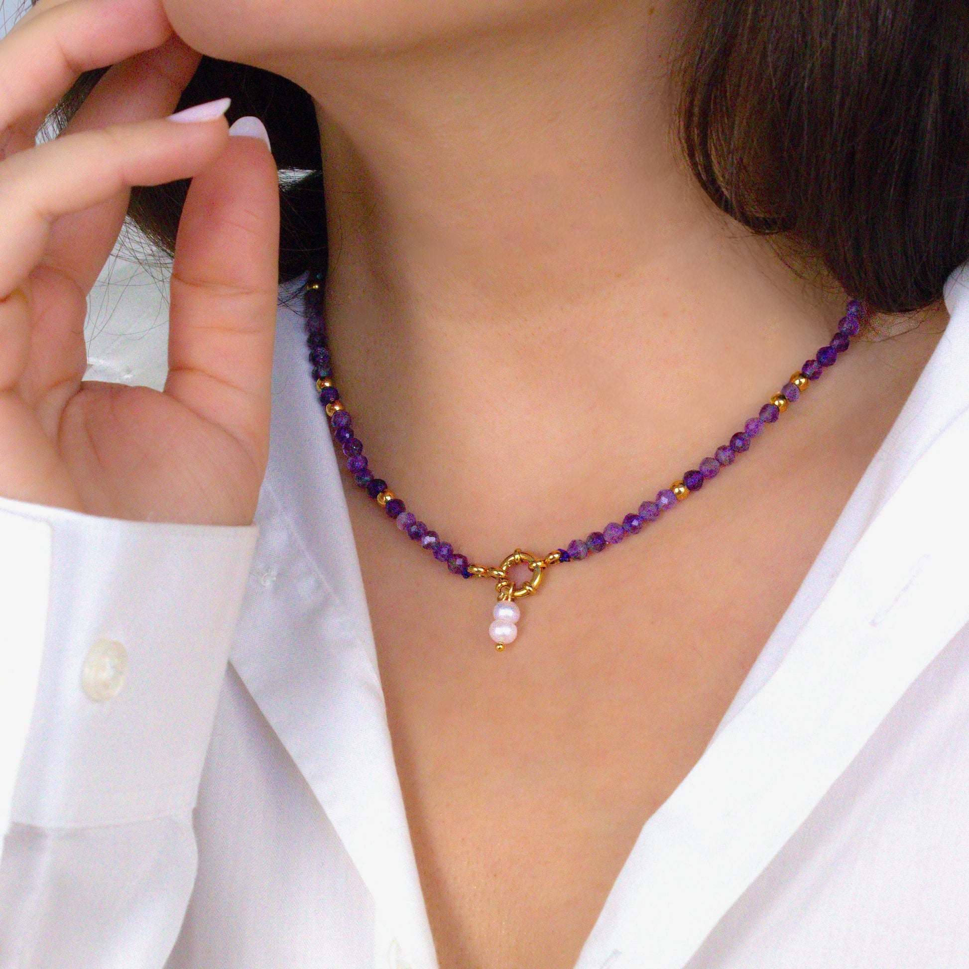 Person wearing a purple beaded necklace with a gold clasp and pearl charm. Amethyst beads.