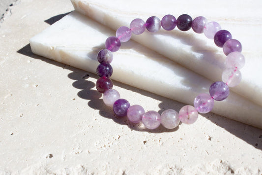 amethyst beaded bracelet with color variation leaning on beige tiles.