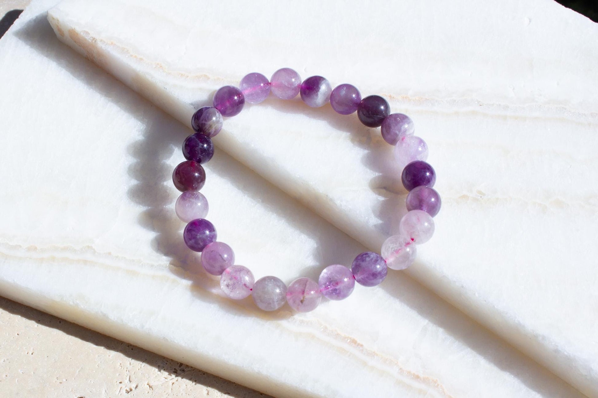 one purple beaded bracelet laying on white tile.