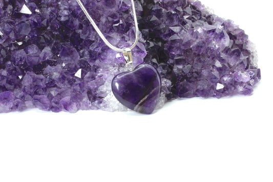 one purple heart pendant leaning against a cluster of amethyst crystal.