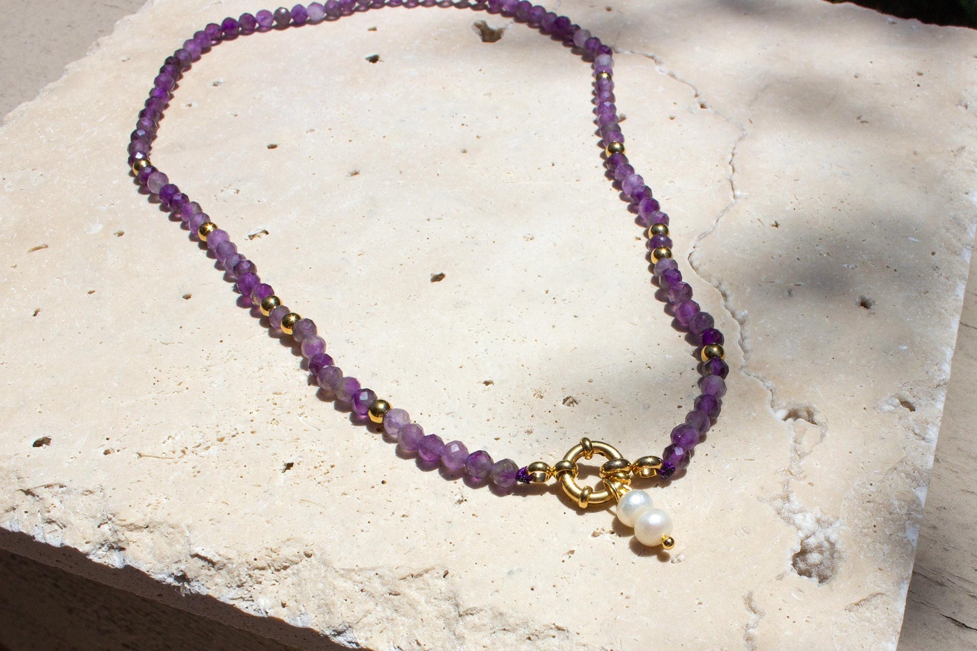 amethyst beaded necklace with gold accents and pearl laying on concrete tile.