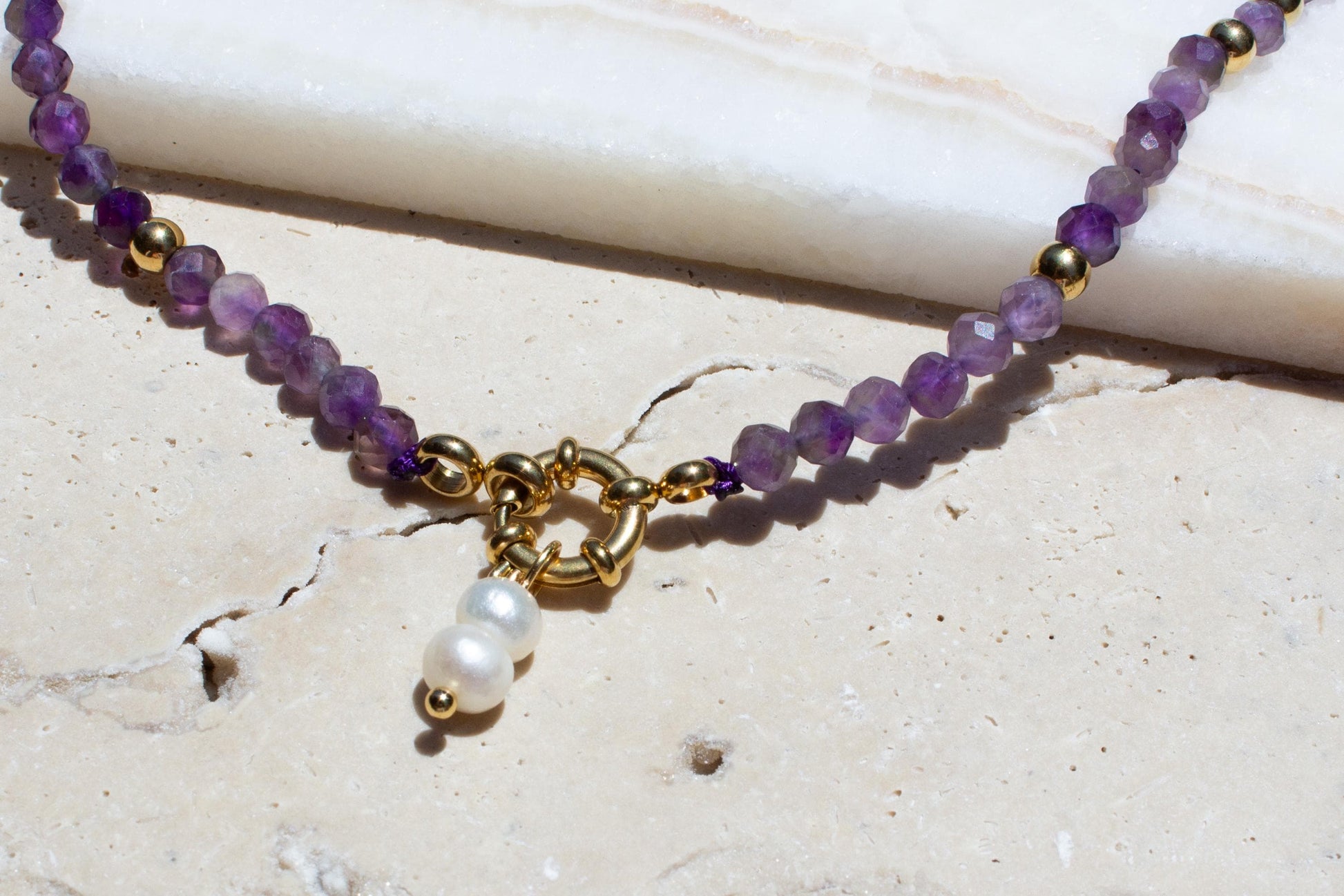 close up of purple amethyst necklace with gold clasp and freshwater pearls on the concrete in the sunshine.