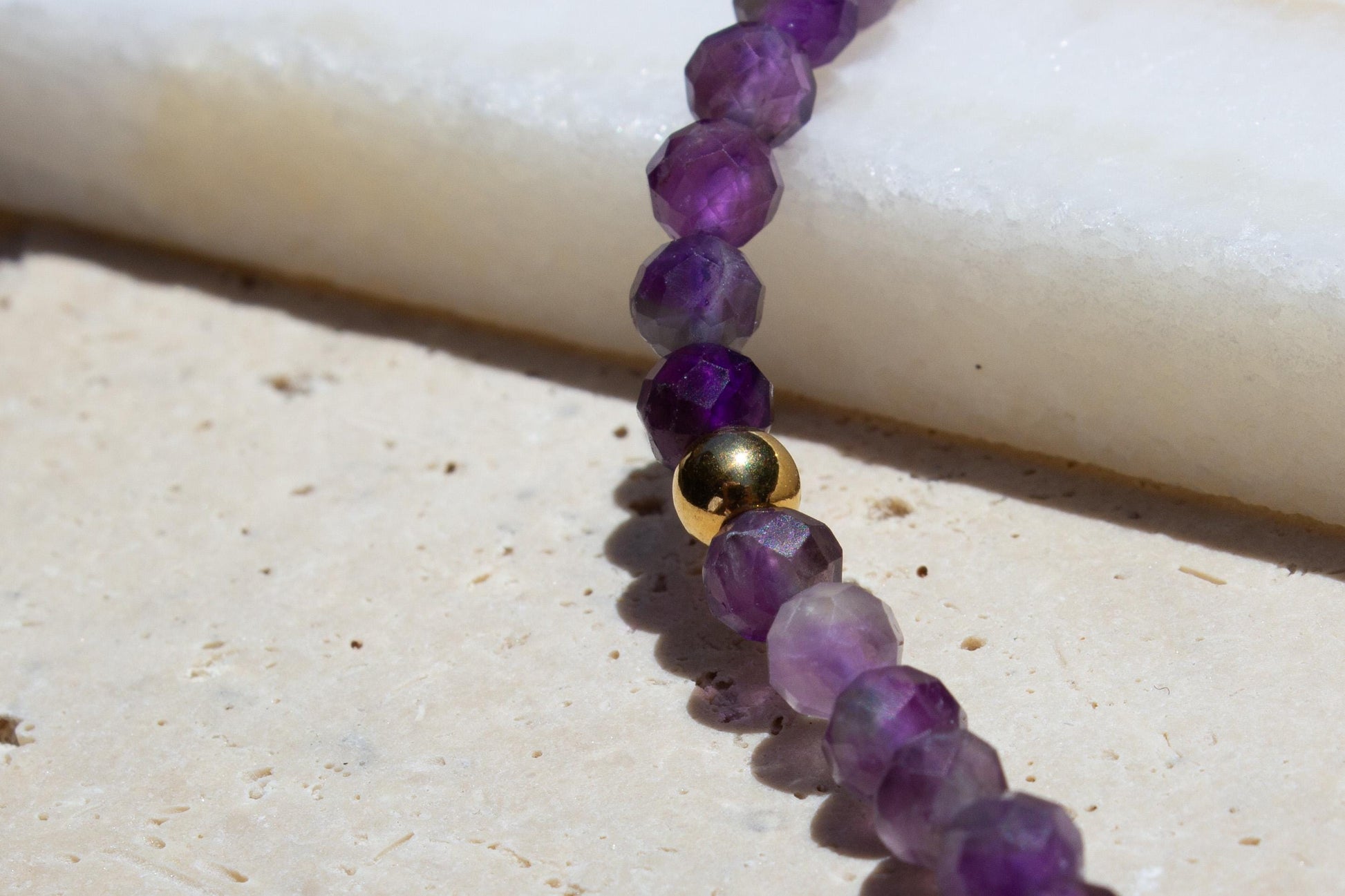 faceted amethyst crystal beads on a necklace with gold bead accent.