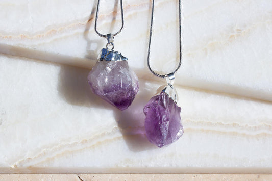 two amethyst purple necklaces on a beige tile background.
