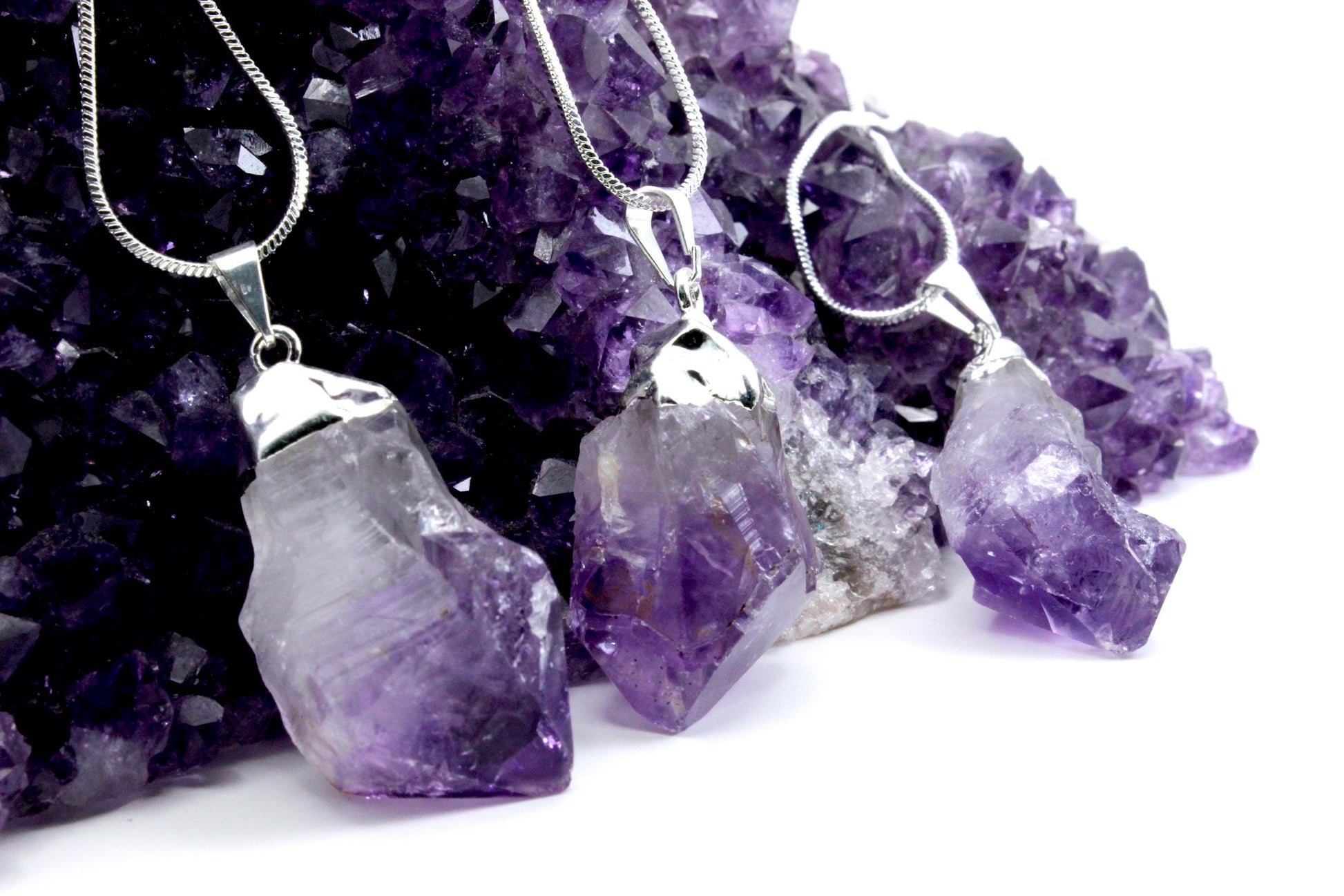 Three purple crystal pendants leaning on a large amethyst crystal.