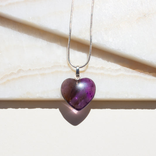 Heart-shaped purple amethyst pendant on a silver chain against a light background.