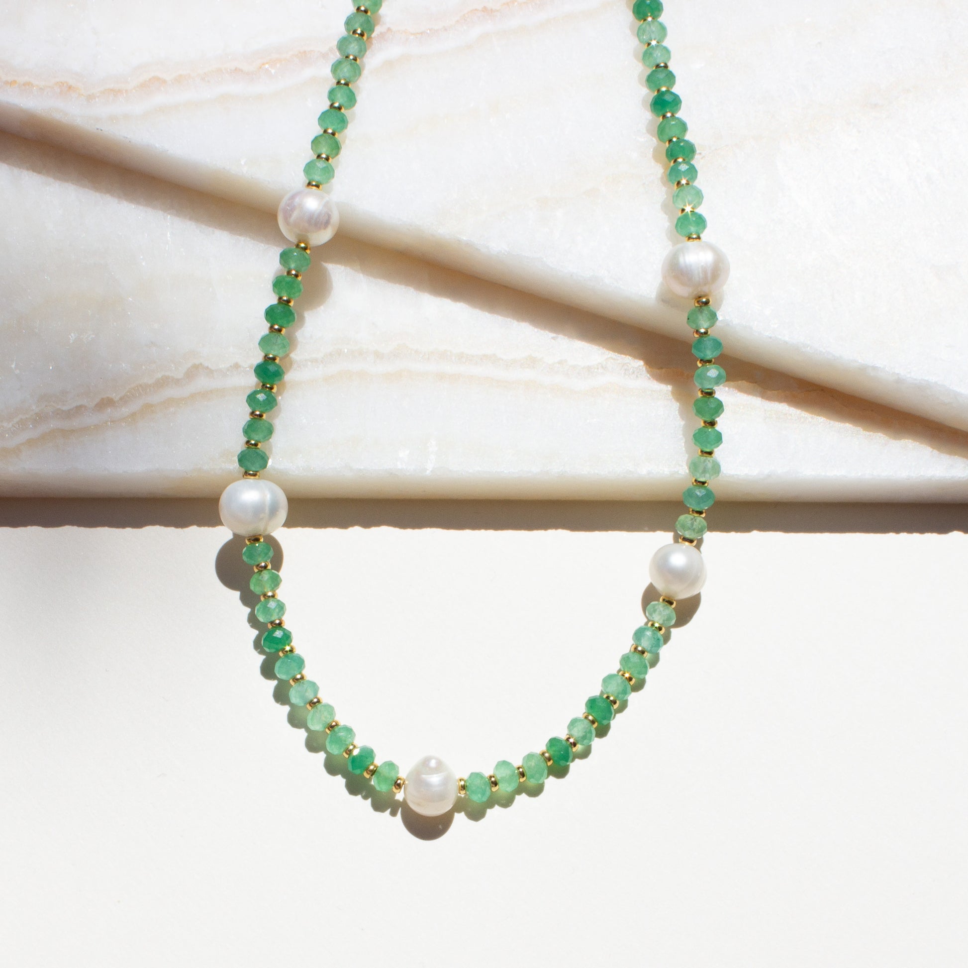 Necklace with green aventurine beads and pearls on a marble surface.