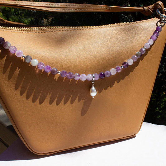 purple amethyst crystal bag charm on a tan handbag. Bag charm comes with a pearl charm.