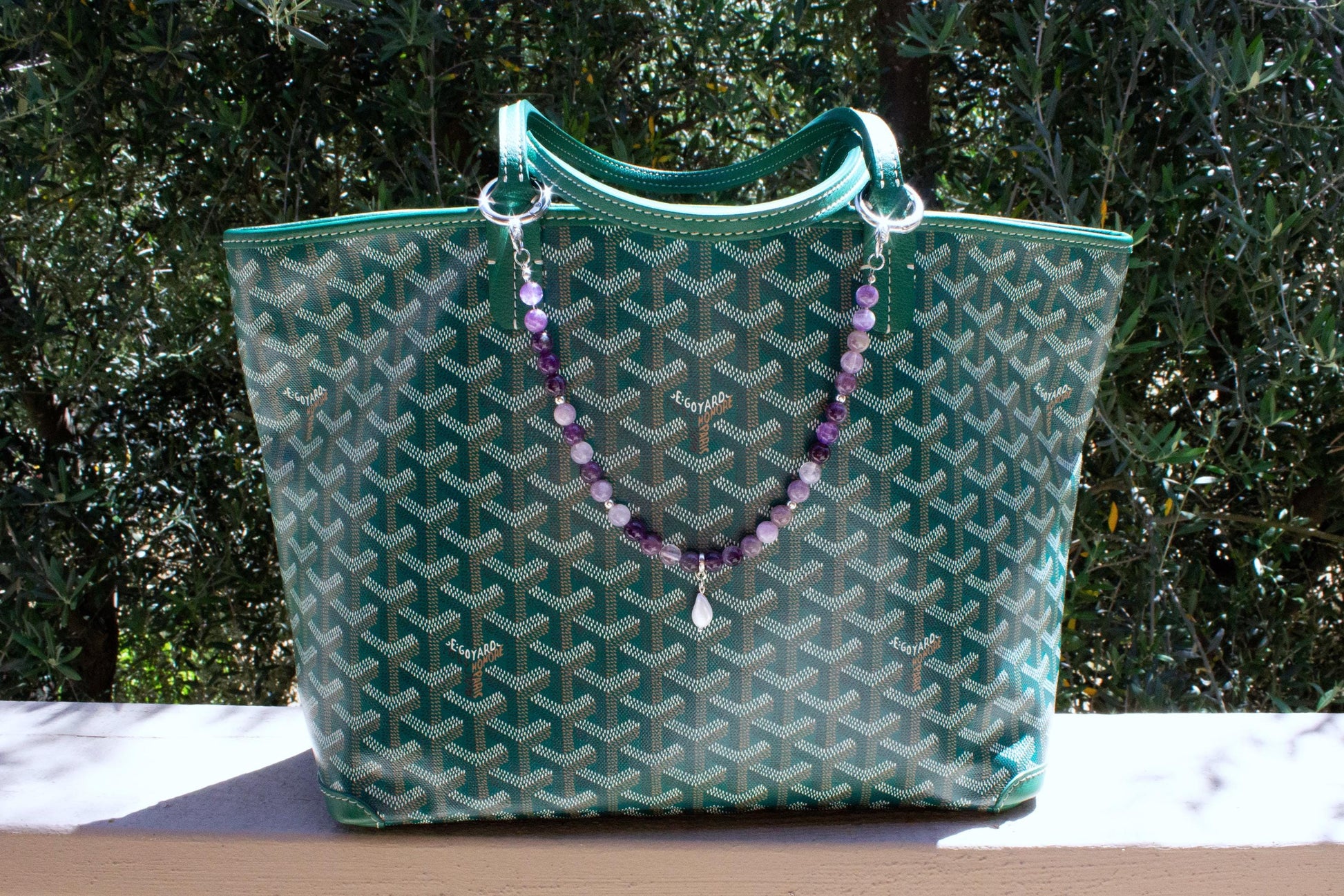 purple amethyst crystal bag charm on a green goyard tote bag.