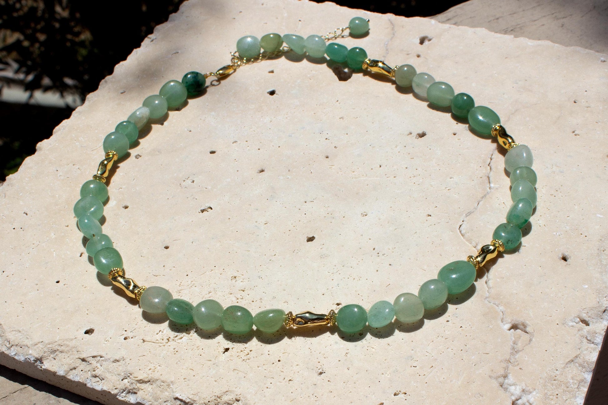 green and gold crystal nucklace on a beige tile.