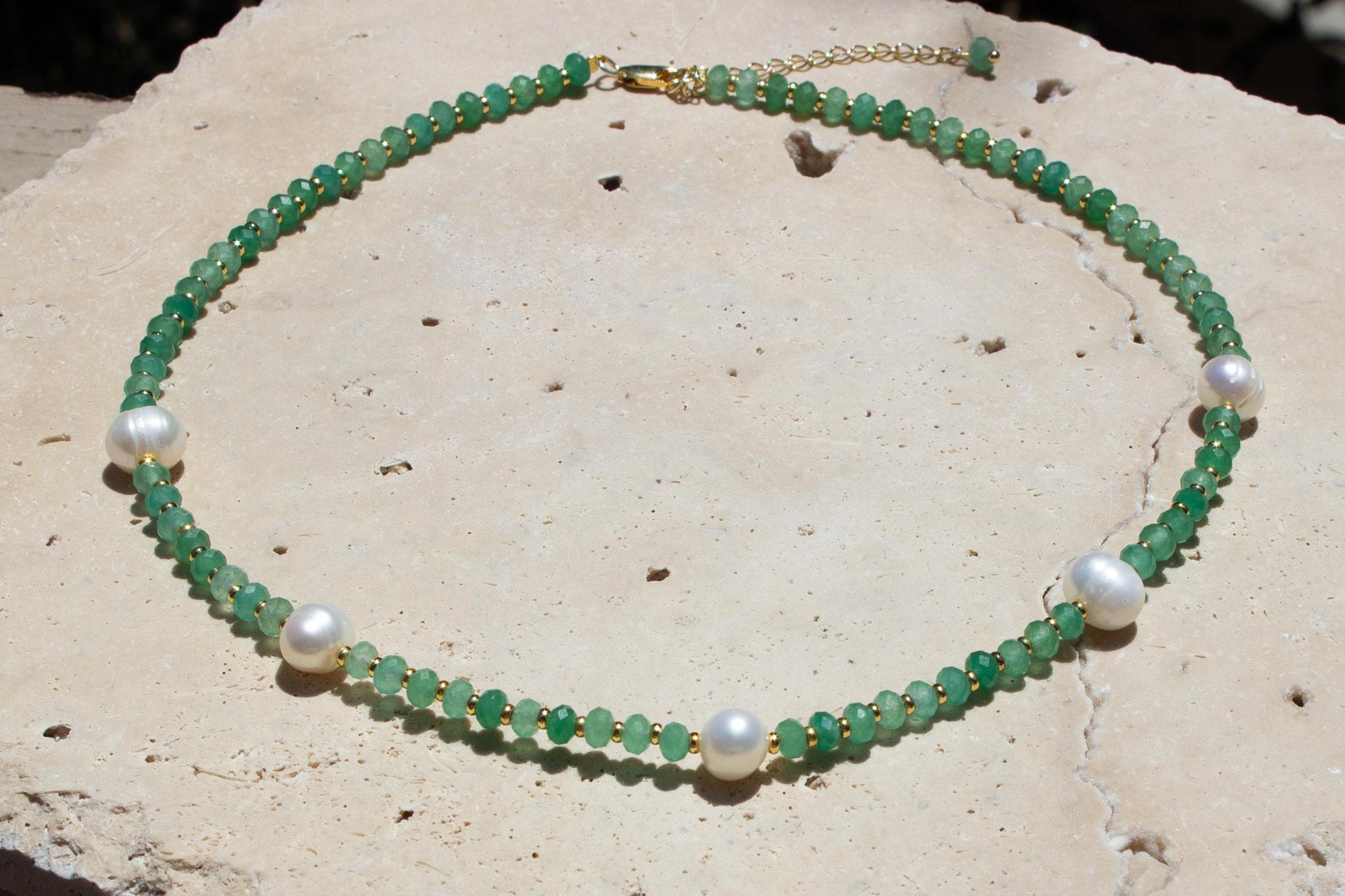 green crystal necklace with gold clasp and freshwater pearl choker on tile outside.