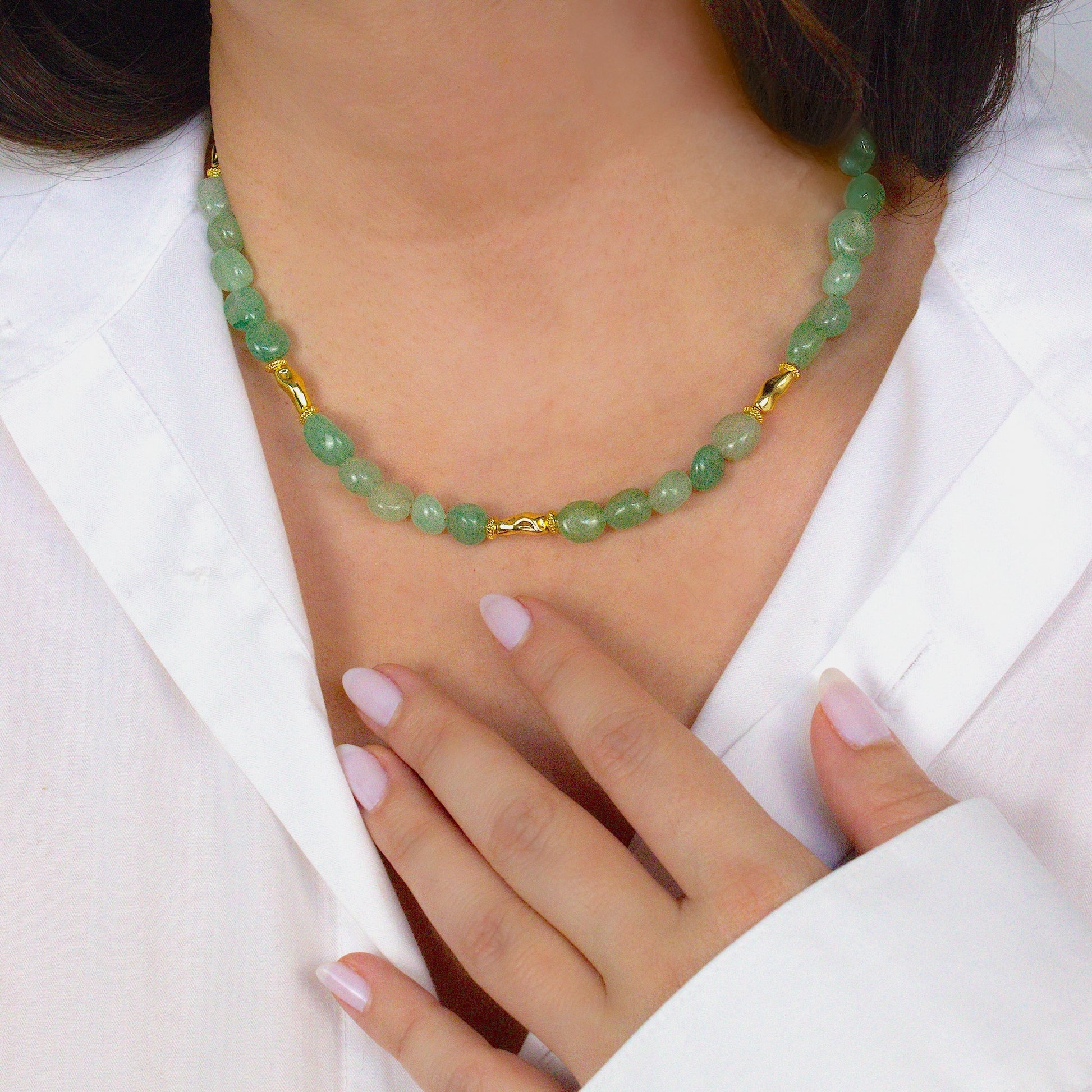 Green beaded necklace with gold accents worn by a person in a white outfit. Green aventurine crystal beads.