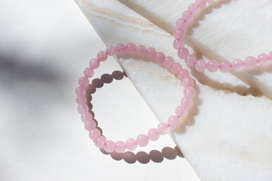 two pink rose quartz crystal bracelets laying on white tiles.