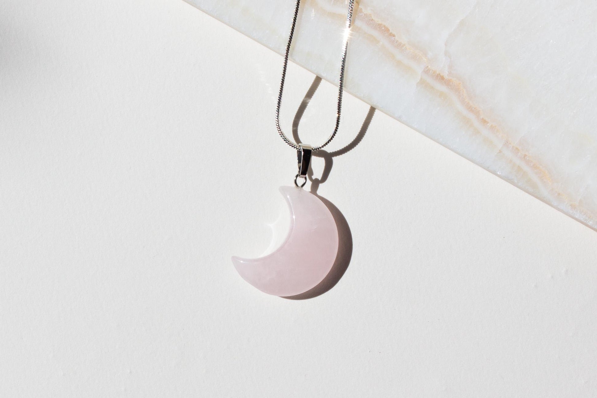rose quartz pink necklace on silver chain laying on white tile.