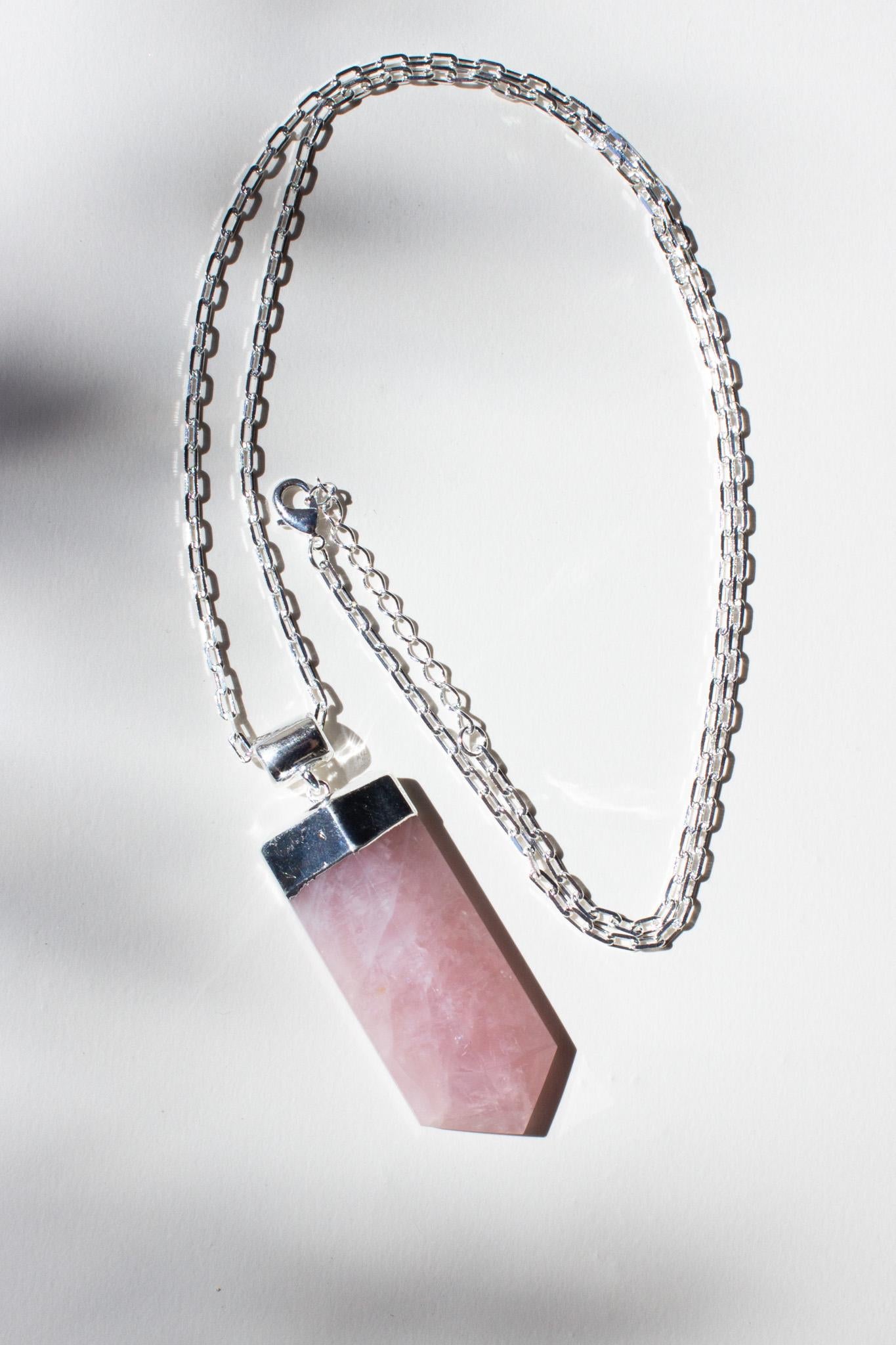 large rose quartz pendant necklace with silver chain laying on the concrete in the sunshine.