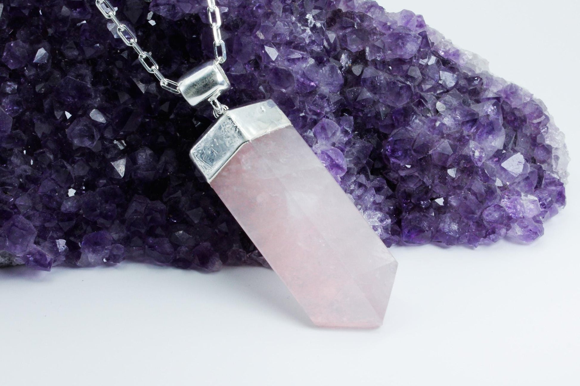 Rose quarts pink pendant crystal laying on purple amethyst crystal.