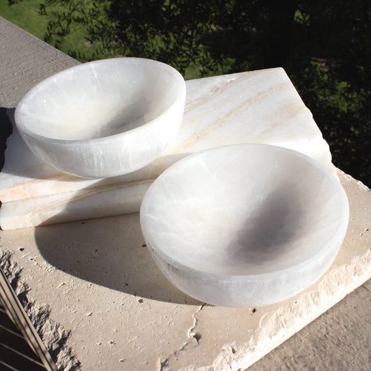 two small white crystal bowls on beige tiles outside.