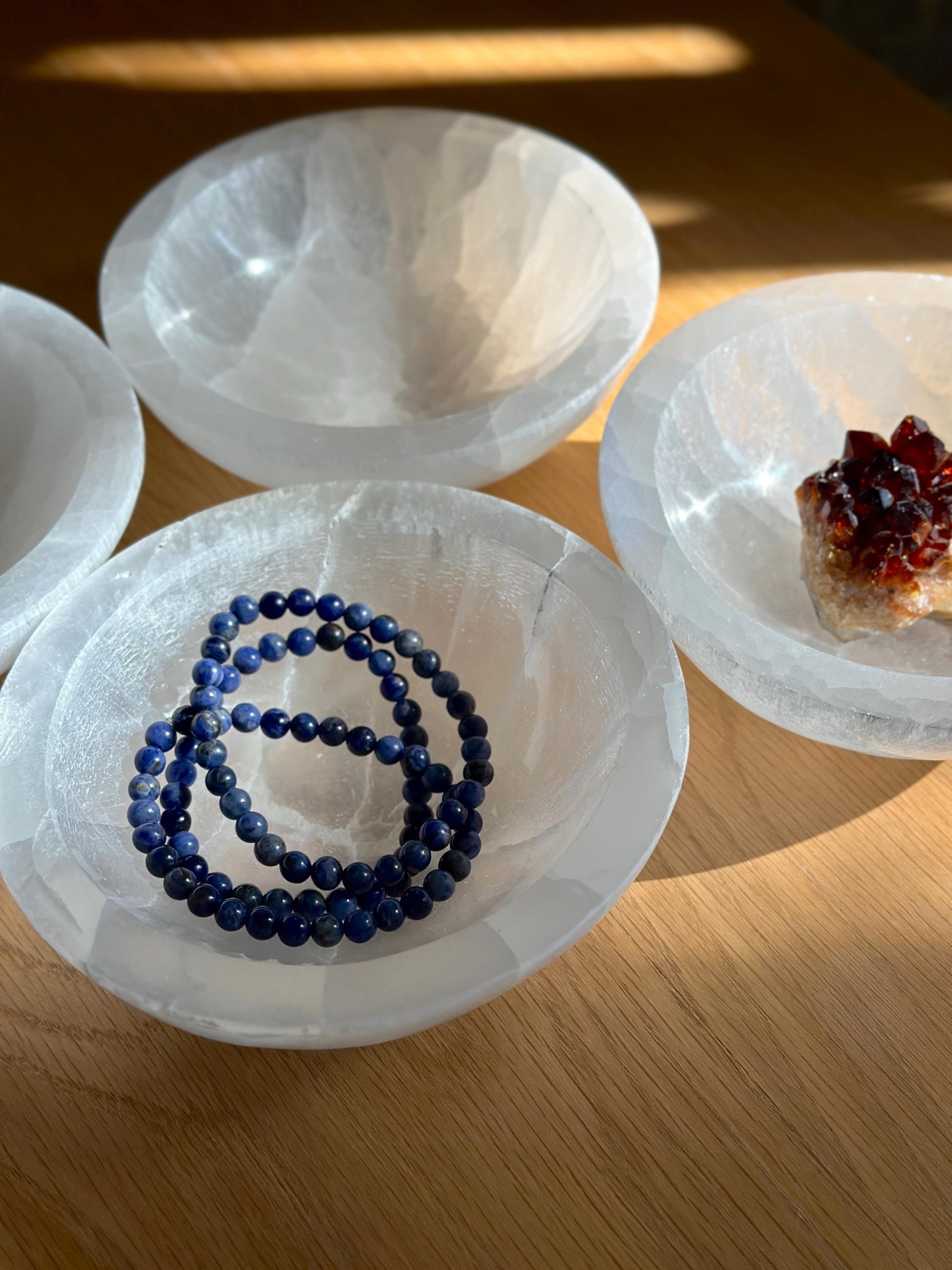 selenite crystal charging bowls holding blue crystal bracelets.
