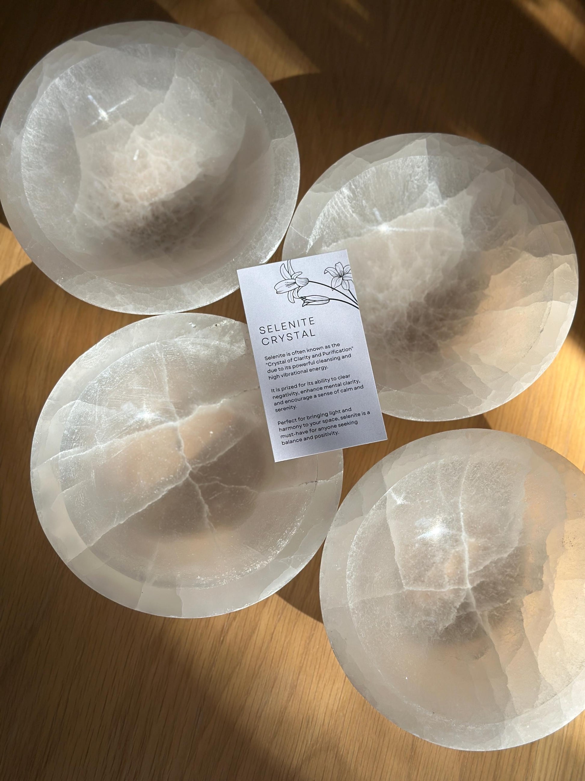 group of 4 white crystal bowls with the a selenite crystal meaning information card on top.