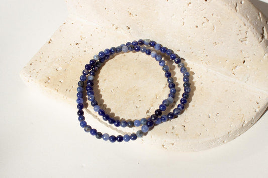 Two blue beaded bracelets laying on a beige concrete tile.