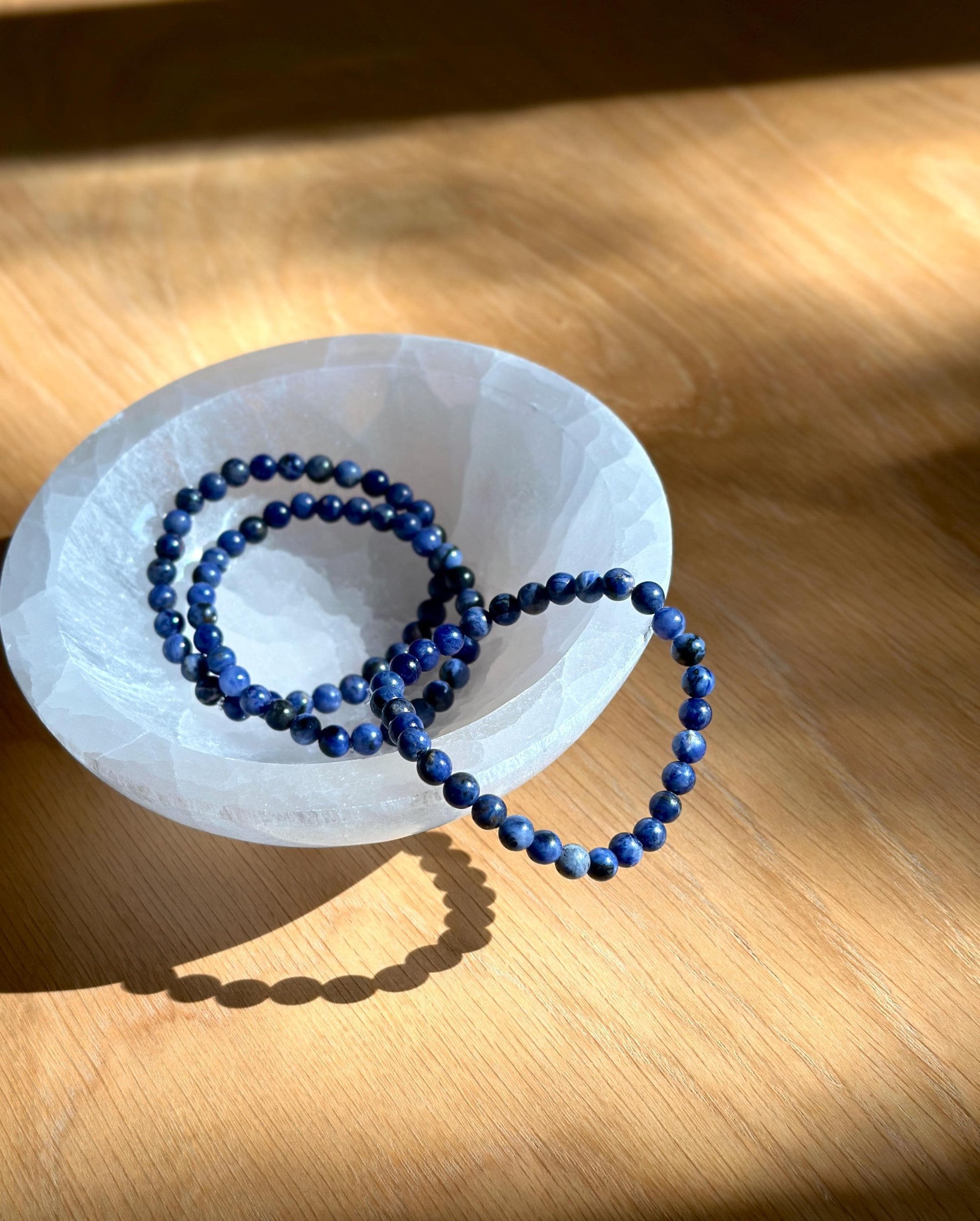 three blue beaded bracelets in a white selenite bowl.