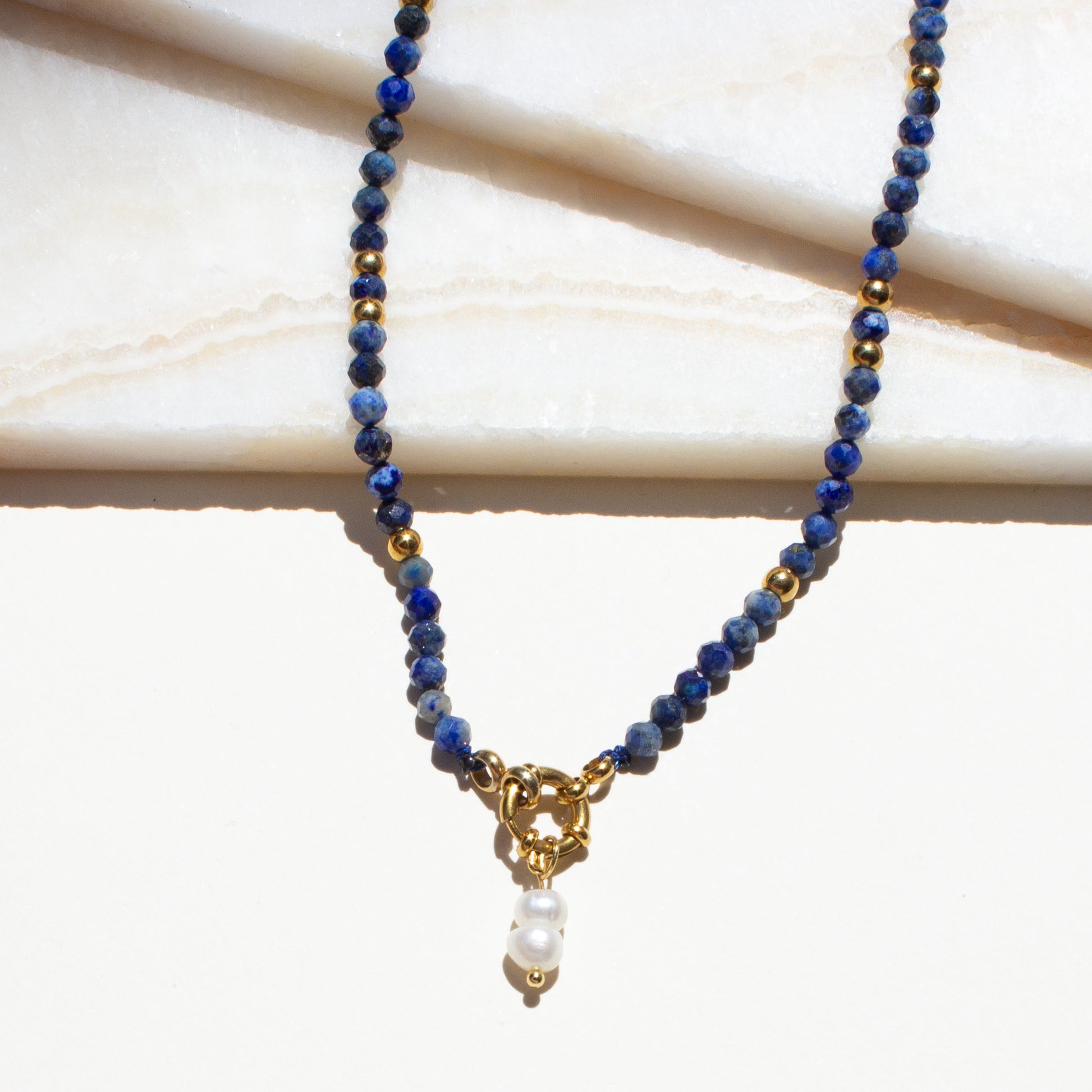Necklace with blue sodalite crystal beads and a gold clasp on a light background.