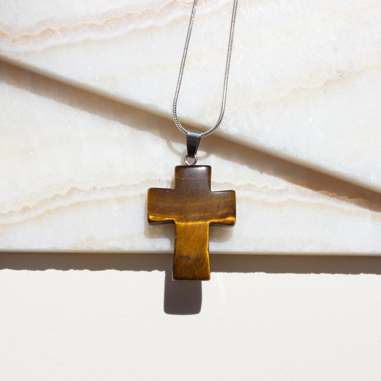 Bronze cross pendant tigers eye on a chain against a marble background.