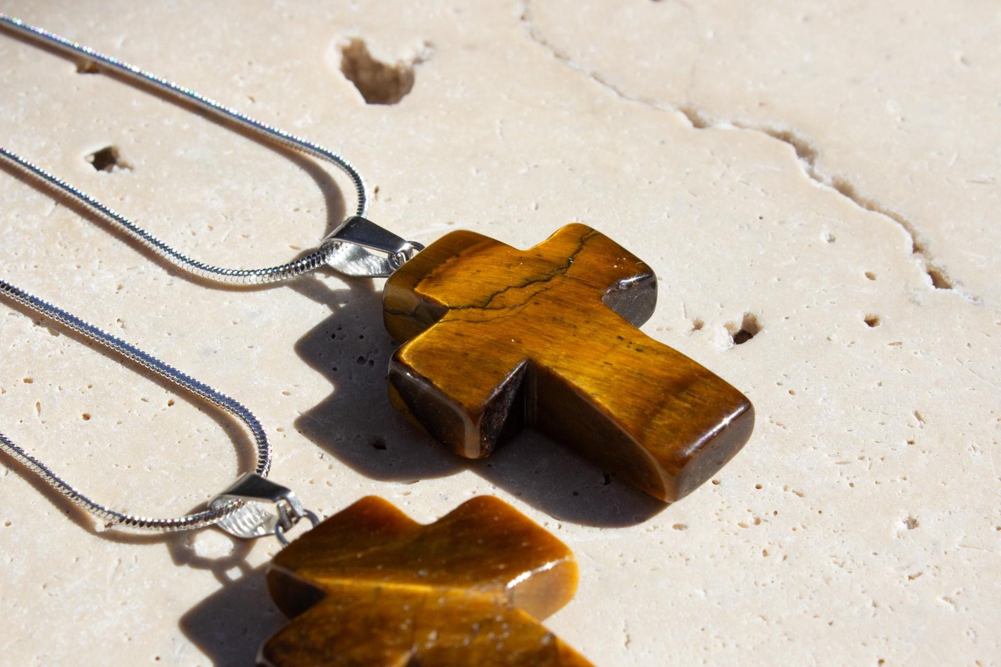 close up of a tigers eye crystal necklace in a christian cross shape on a silver chain.