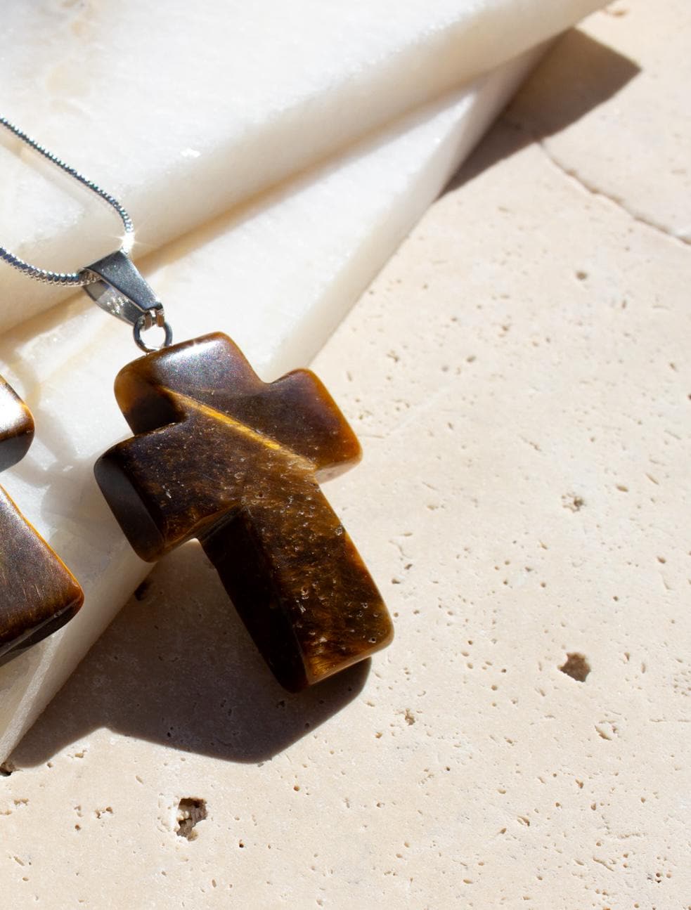 close up on a brown cross shining in the sunshine on a silver chain.