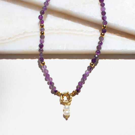 Purple amethyst beaded necklace with a gold clasp and pearl accent on a white background.
