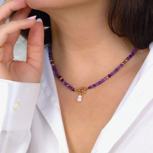 Person wearing a purple beaded necklace with a gold clasp and pearl charm. Amethyst beads. 