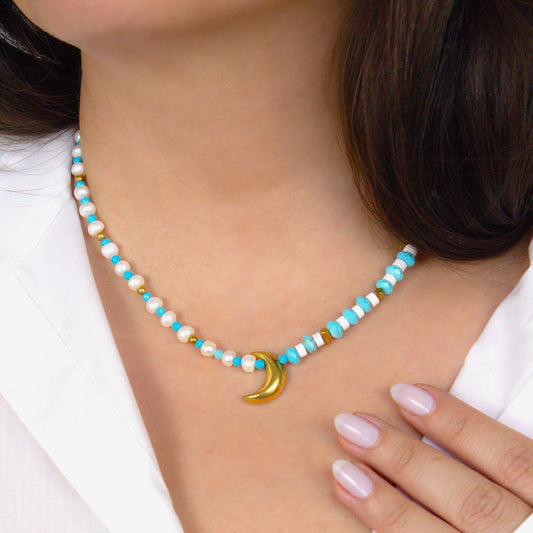 Necklace with a crescent moon charm worn by a person in a white shirt. Beads made from genuine turquoise and pearl eads.