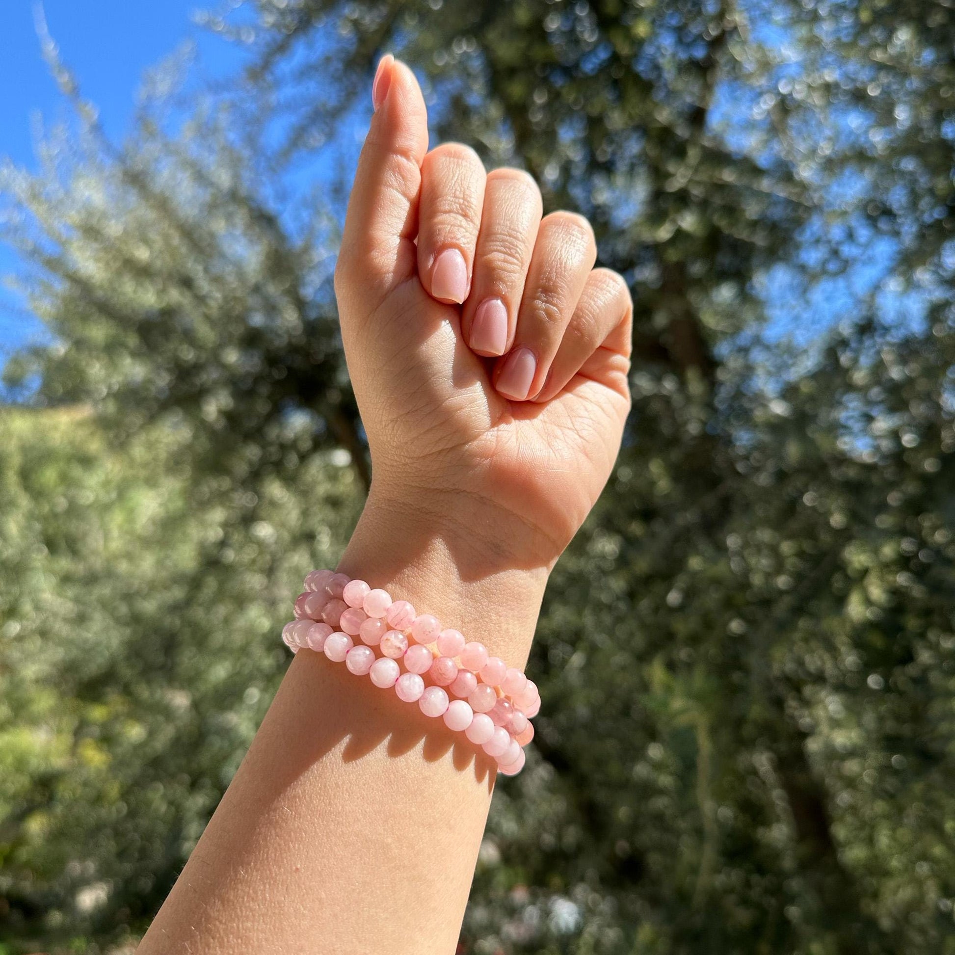 girl wearing three pink crystal rose quartz bracelets outside. 