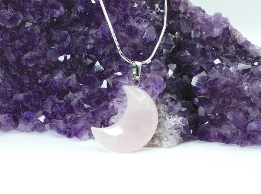 pink rose quartz moon necklace leaning against a purple amethyst crystal. 
