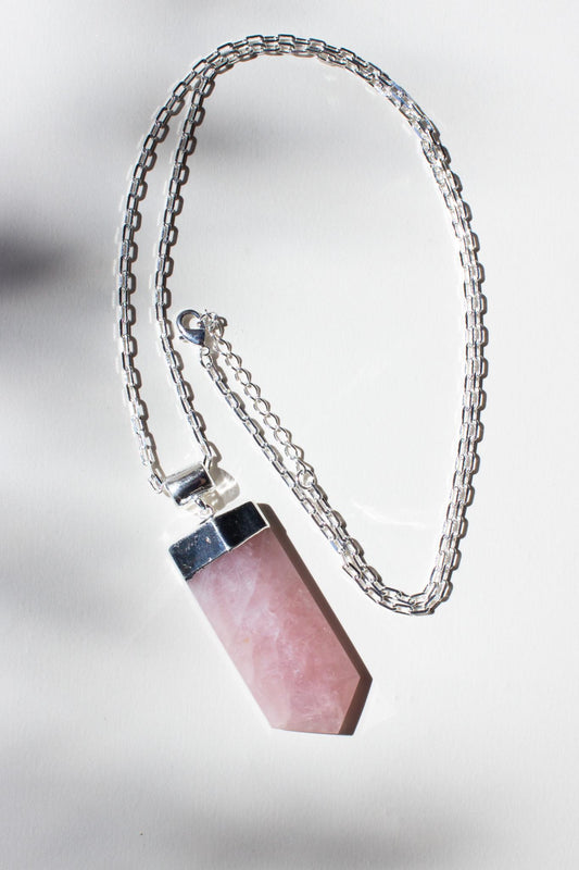 large rose quartz pendant necklace with silver chain laying on the concrete in the sunshine. 