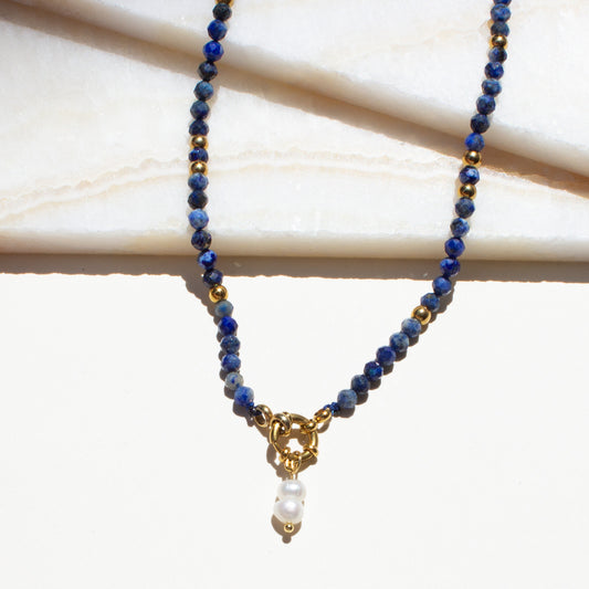 Necklace with blue sodalite crystal beads and a gold clasp on a light background.